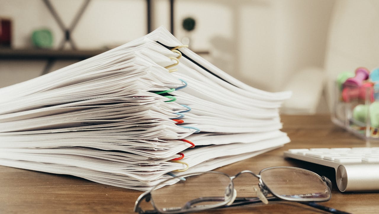 why-choose-us Close-up of a stack of office papers on a desk with glasses, emphasizing organization.